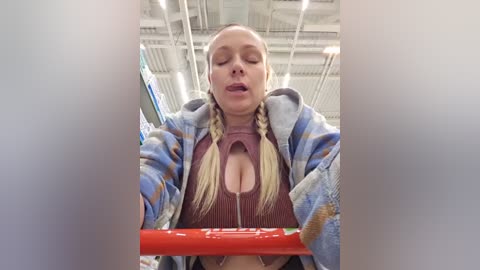 A video of a blonde woman with pigtails, wearing a low-cut top revealing cleavage, pushing a red shopping cart in a dimly lit store.