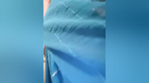 Video of a person wearing a blue surgical gown, with the fabric draped over their upper body, emphasizing the folds and creases. The background is a solid blue, possibly a hospital setting.