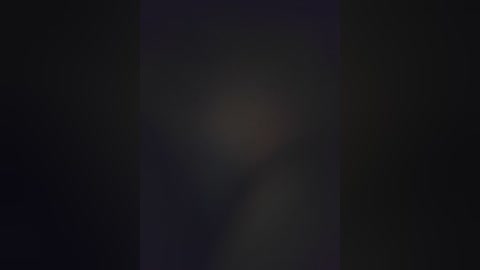 A dimly lit, grainy video with a central, indistinct, blurry figure, likely a person, against a dark background. The image is low-resolution and lacks clear details, making identification difficult.