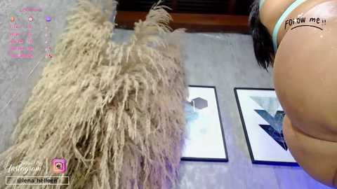 Video of a woman with dark hair and a tattoo, holding a feather duster, standing next to a wall with abstract art.