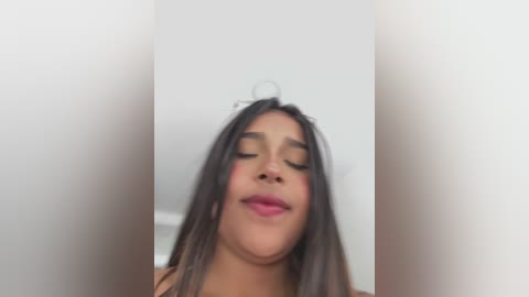 Video of a smiling, medium-skinned woman with long, straight black hair, wearing pink lipstick, against a white background, with slightly blurred edges.