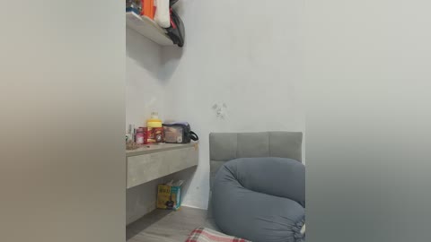 Video of a small, cozy room with a beige bean bag chair, a minimalist white shelf, and a few scattered items on the floor, including a yellow box and a red container. The walls are plain white, giving the space a clean, minimalist feel.