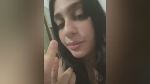 Media: Video of a young woman with dark hair, light skin, and a slight smile, making a peace sign with her fingers, partially obscured by out-of-focus hands.
