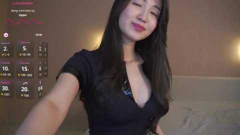 A video of an Asian woman with long black hair, wearing a black dress, smiling, in a dimly lit room with a digital clock displaying 15:45.
