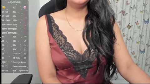 Video of a woman with long black hair wearing a burgundy camisole with black lace, seated in front of a computer displaying temperature and humidity readings.