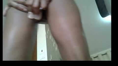 A blurry, low-angle video showing a close-up of a light-skinned person's hand holding a penis, with a partially visible vagina in the background. The setting appears to be a bathroom with a white wall and a door.