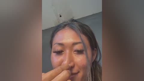 Video of an Asian woman with long, straight dark hair, light skin, and closed eyes, with a man's finger gently touching her nose, set against a neutral indoor background.