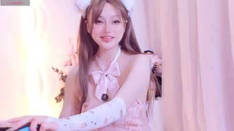Video of an East Asian woman with long, light brown hair, wearing a pink, lacey dress with white fur accents, smiling.