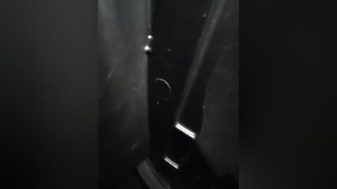 A dimly lit, high-contrast video captures a close-up view of a black, cylindrical object with a reflective surface, possibly a metal pipe or rod, partially submerged in a dark liquid. The lighting creates a moody, mysterious atmosphere.