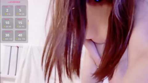 Media: Video of a woman with long brown hair, partially obscured by her hand, lying on a bed with a white sheet, and a Love Live! smartphone screen showing her daily schedule.