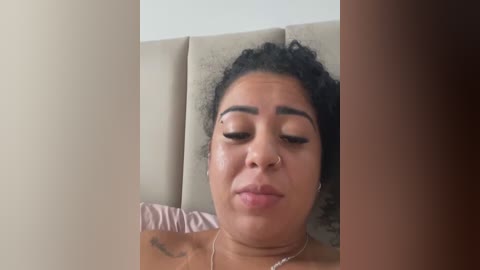 Video of a young Black woman with curly hair, closed eyes, and a neutral expression, lying on a beige cushioned headboard.