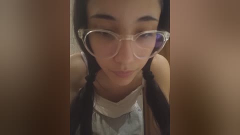 Video of an Asian woman with long black hair, wearing large clear glasses and a white floral-patterned dress. She has a soft, contemplative expression.