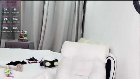 A video of a modern bedroom with a white leather chair, a white bed, a TV screen displaying a fitness app, and scattered workout gear.