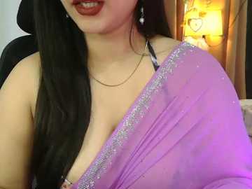 Media: A video of a South Asian woman with fair skin, long black hair, and a deep red lipstick smile, wearing a pink sari with silver embroidery, a black bra strap peeking out, and a gold necklace.