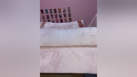 Video of a cozy, pastel-colored bedroom with a pink wall adorned with a collage of colorful photos, featuring a white sofa with plush cushions and a fluffy white blanket.