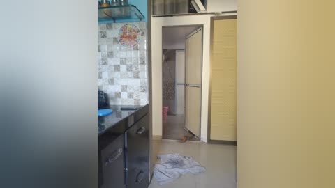 A video of a narrow hallway with a bright yellow wall, a tiled backsplash, a black kitchen counter, and a white cloth on the floor.