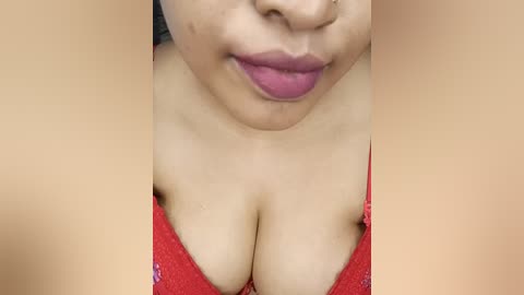 Video of a woman with light brown skin, wearing a red sequined bra, emphasizing her large, cleavage-revealing breasts. Her full lips are slightly parted. The background is out of focus.