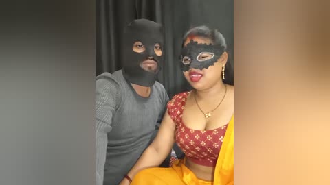 Media: Video of a man in a black mask, gray shirt, and a woman in a red floral blouse with a yellow sari, both smiling against a black backdrop.