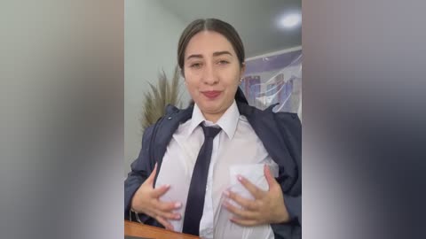 Video of a Latina woman with long brown hair, wearing a white shirt and dark tie, holding two cups, smiling, in a modern office setting.