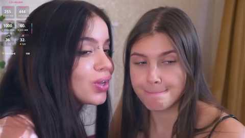 Media: Video of two women with long, straight black hair, one with light skin and glasses, the other with medium skin, smiling, in a cozy, dimly lit room.