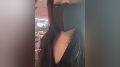 A close-up video of a woman with long black hair, wearing a black face mask and a black top, partially visible in a dimly lit, modern store.