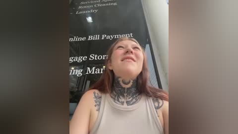 Video of a smiling young woman with long brown hair, wearing a sleeveless top, standing in front of a window with text about \"line billing\" and \"ing Mar.\