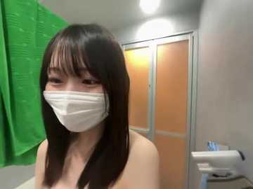 Video of an Asian woman with long black hair, wearing a white mask and a light-colored top, standing in a bathroom with a green shower curtain, orange-tiled shower, and a white toilet.