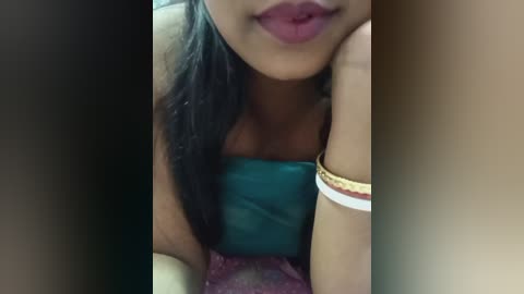 Video of a young woman with medium brown skin, long black hair, and full lips, wearing a teal strapless top, lying on a bed.