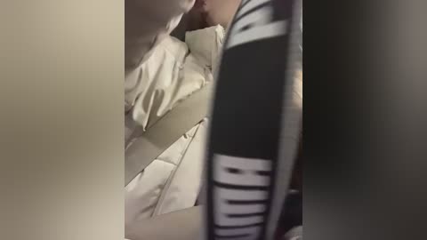 A video capturing a close-up view of a person's torso in bed. The individual is wearing a black and white striped shirt with a graphic design. The bedding is white and slightly rumpled.