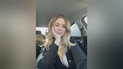 Video of a young woman with fair skin and long, wavy blonde hair, wearing a black cardigan, seated in a car with a leopard-print jacket and a gray interior.
