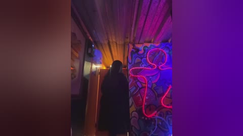 Video of a narrow, dimly lit hallway with neon pink and purple lights on the right wall, creating an eerie, surreal atmosphere. A silhouette of a person in a black coat is visible in the background.