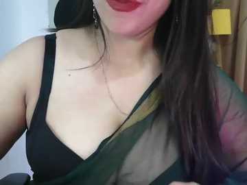 Media: Video of a woman with fair skin, long dark hair, and red lipstick, wearing a black bra and sheer green sari, indoors.