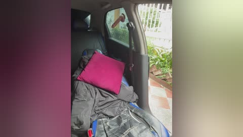 A video of a car interior showing a pink pillow on a black blanket, with a man's arm hanging out of the open door.