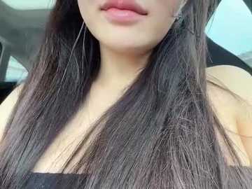 Video of a light-skinned woman with long, straight, dark brown hair, wearing a black top, seen from the shoulders down, lips slightly parted, and wearing dangling silver earrings.