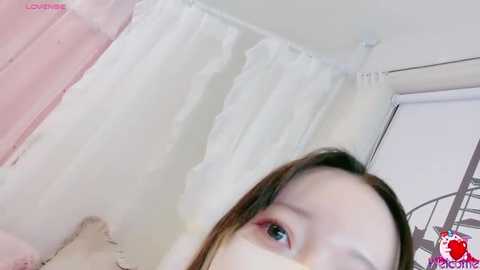 Video of a young Asian woman with fair skin, brown hair, and pink eyeshadow, partially obscured by a pink shower curtain.