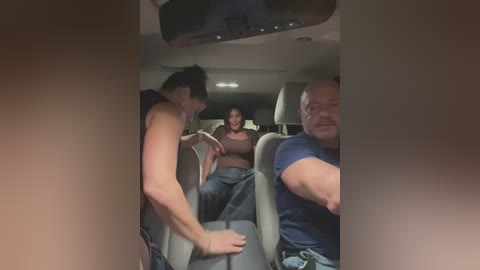 Video of three people in a car: a shirtless man in the foreground, a woman in the middle, and a bald man in the background. The car's interior is dimly lit.