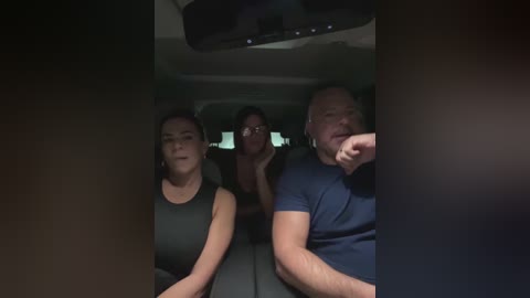 Video of three people sitting in a car at night: a woman with dark hair and glasses in the middle, a man with short hair on the right, and another man with glasses on the left.