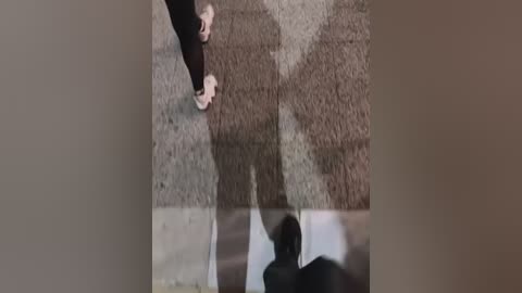 Video of a person's feet in black shoes, standing on a concrete floor, casting a shadow. The background is a blurred, beige wall.