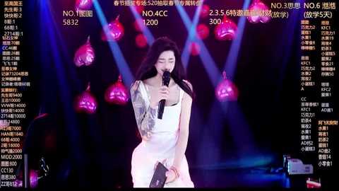 Video of an Asian woman with long black hair, singing into a microphone on stage. She wears a white dress with silver sequins. The background features a dimly lit stage with pink and purple lights, and a large screen displaying Chinese text.