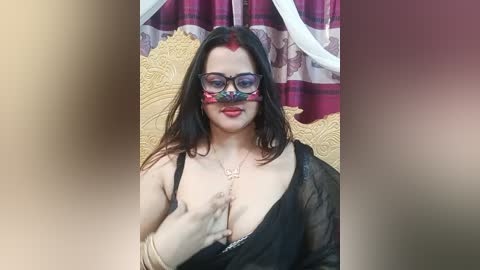 A video of a fair-skinned woman with long dark hair, wearing a black see-through blouse revealing cleavage, and a colorful mask covering her nose and mouth, seated on a gold throne with red curtains in the background.