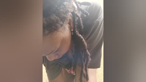 Video of a young Black woman with braided hair, wearing a dark shirt, leaning over with her eyes closed, in a dimly lit room with beige carpet.