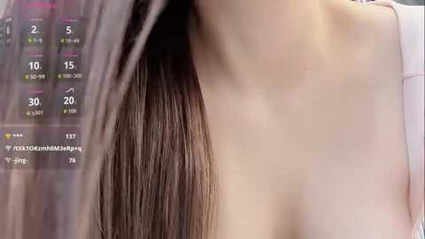 A close-up video of a woman's bare, pale skin with long, straight brown hair cascading down the left side. The background includes a digital display showing various numbers and symbols. The image appears to be taken in a modern, indoor setting.