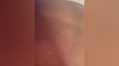 A video captures the smooth, light brown skin of a person's thigh, likely a woman, with a small, faint blemish visible. The background is a gradient of warm colors, suggesting a soft, natural light source.