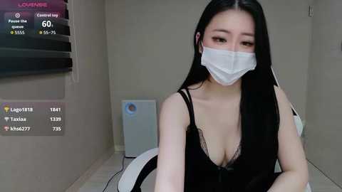 Video of an East Asian woman with long black hair, wearing a black lace bra and white face mask, sitting on a toilet in a small, dimly lit bathroom with a white heater.