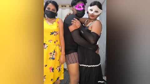 Video of three women in Halloween costumes: one in a yellow dress with a floral pattern, one in a black outfit with a white mask, and the third in a black dress with a white mask, standing in a dimly lit room.