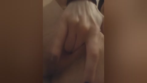 Video of a person's hand holding their genitals through sheer fabric. The background is blurred, with warm, brownish hues. The hand appears to be Caucasian, with visible veins and nails. The image conveys a sense of vulnerability and intimacy.