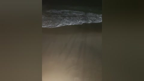 A video showing a close-up of a rock formation with a jagged, dark edge and a smooth, lighter-colored surface, set against a blurry, dark background.