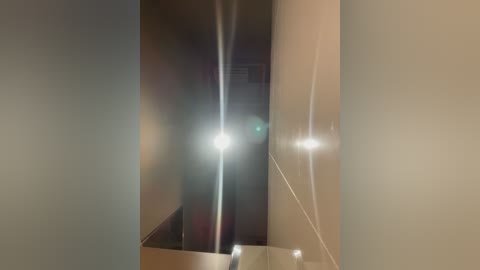 Video of a dimly lit, narrow corridor with beige walls and a greenish lens flare at the center. The corridor's smooth, matte texture contrasts with the sharp, reflective lens flare.