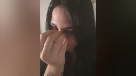 A close-up video of a woman with long, straight black hair, covering her eyes with her left hand. Her facial expression is somber. The background is dark and blurry, emphasizing the subject's emotional state.