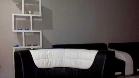 A video of a minimalist living room with a white leather couch, a modern white geometric shelving unit, and a gray wall.